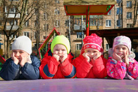 4 kids bundled in winter coats on the playground lean on their hands, listening thoughtfully