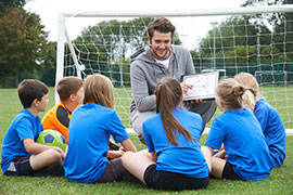 Group of young soccer players surrounding their coach in front of a net