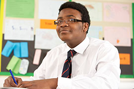 Young man in shirt and tie sitting at school desk attentively awaits instructions